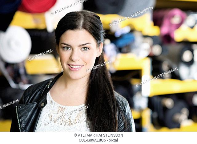Portrait of young seamstress in front of textile shelves in workshop