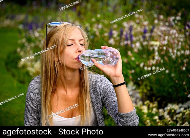 Fit woman drinking water from a bottle in a park or garden in London, United Kingdom