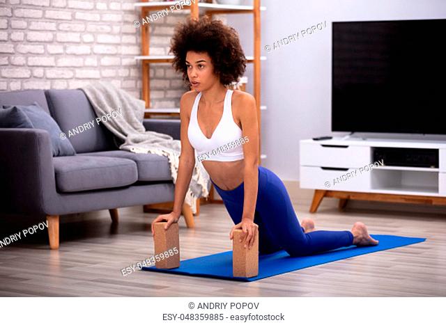 Fit Young Woman Using Wooden Blocks While Doing Exercise On Yoga Mat In Living Room