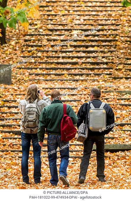 22 October 2018, Berlin: Three men stand near the main station in front of a staircase covered with colourful autumn leaves