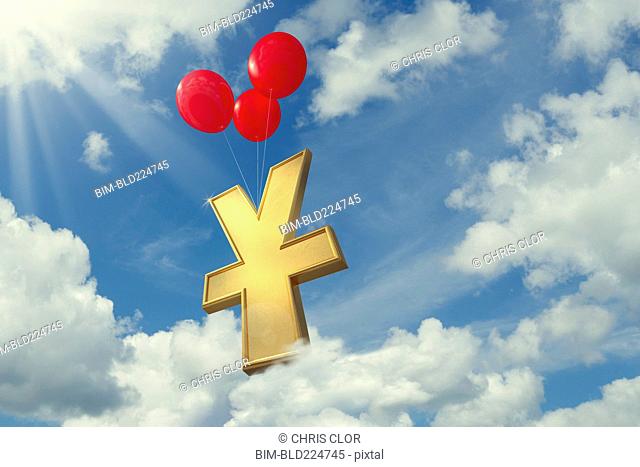 Red balloons lifting yuan symbol in cloudy sky