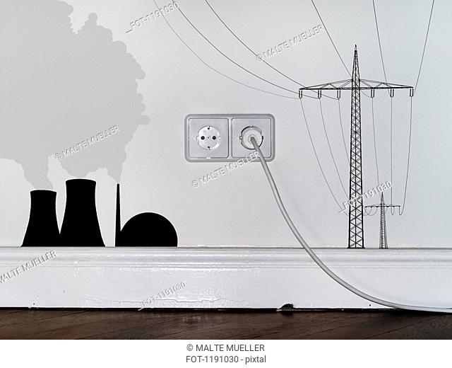 A plug in an outlet in between decals of a nuclear power station and electricity pylons