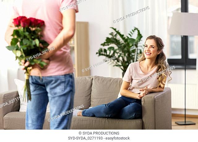woman looking at man with bunch of flowers at home