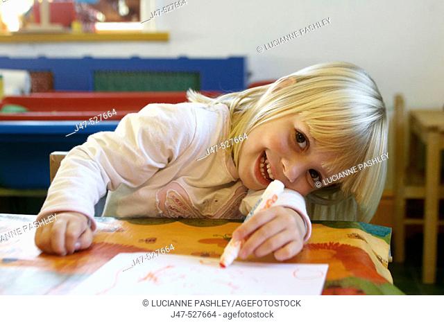 4 year old girl smiling into camera at nursery, drawing