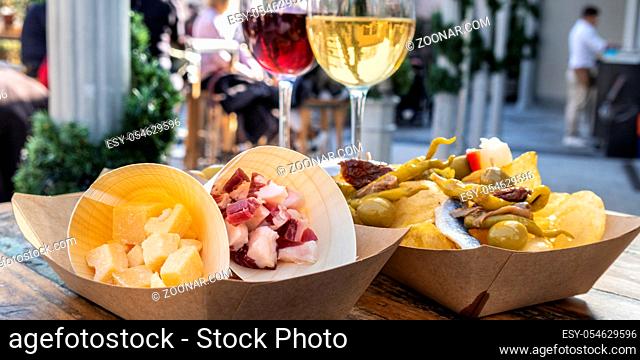 Tapas bar panorama. Cheese, ham and pinchos with red and white wine on a wooden table in an outdoors cafe