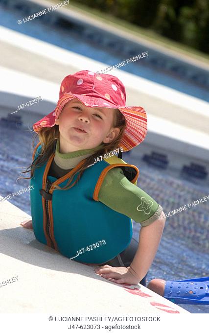 4 year old girl leaning out of the pool on holiday, smiling into camera