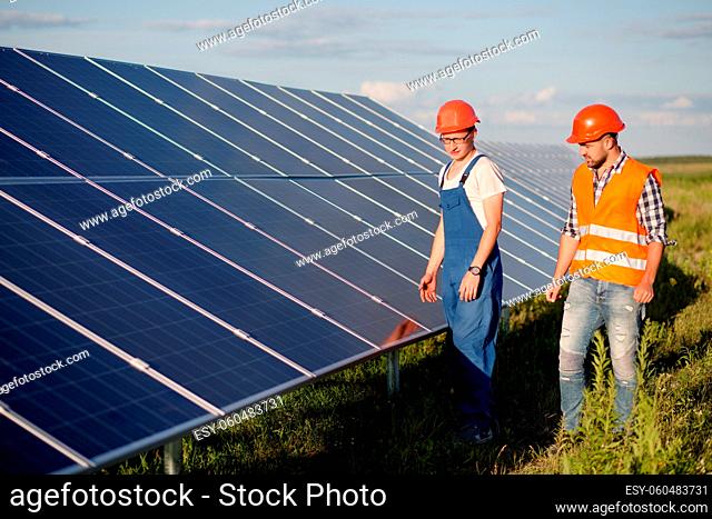 View on photovoltaic panels of solar power station. Foreman and technician looking at solar energy panel