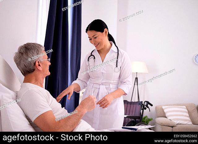 Sweet asian doctor checking up on patient. Smiling asian nurse with stethoscope around her neck checking up on elderly patient