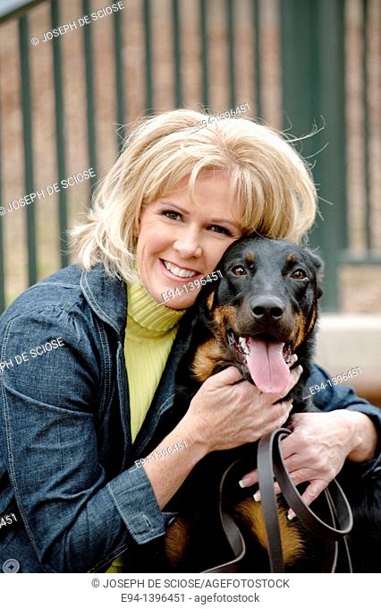 Fifty year old blond woman hugging a Doberman Pinscher on a stairway in a park
