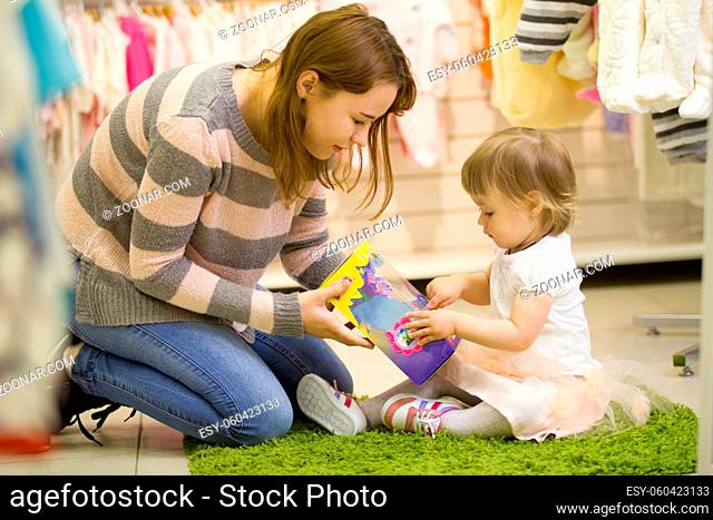 Young mother with little daughter playing with toys at the children's shop, telephoto shot