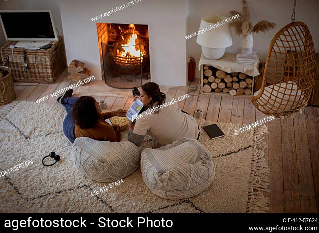Mother and daughter relaxing with digital tablet by fireplace