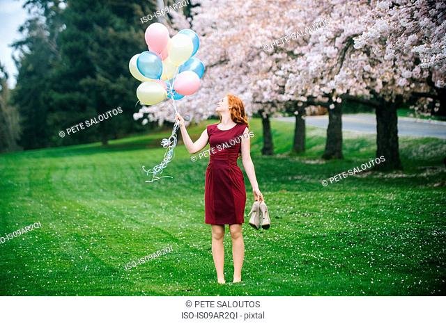 Young woman holding bunch of balloons in spring park