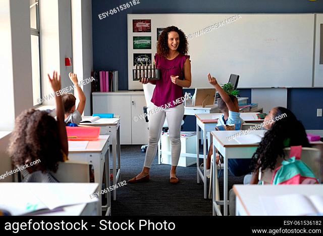 Caucasian young female teacher looking at multiracial elementary students raising hand during class