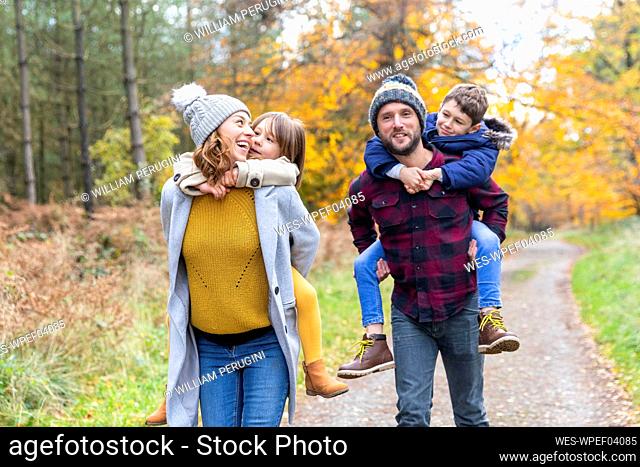 Parents piggybacking children while walking in forest during autumn