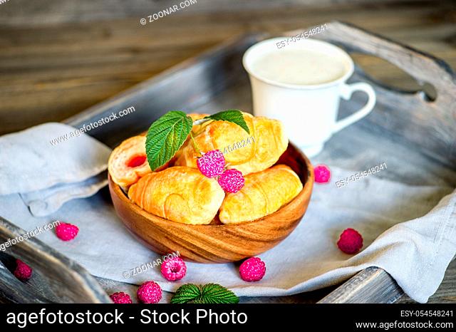 Croissants with raspberries on a wooden tray. The concept of a wholesome breakfast