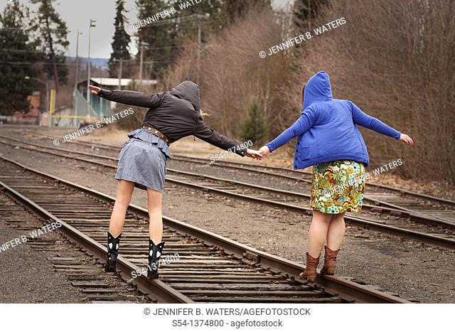 Two young women walking together on railroad tracks