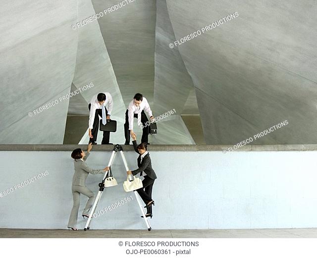 Two businessmen helping two businesswomen up ladder in structure