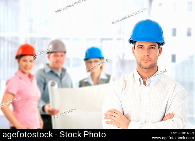 Architect in hardhat standing with team holding plan in office