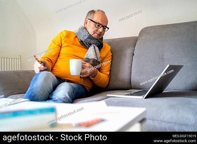 Man holding cup watching laptop on sofa at home