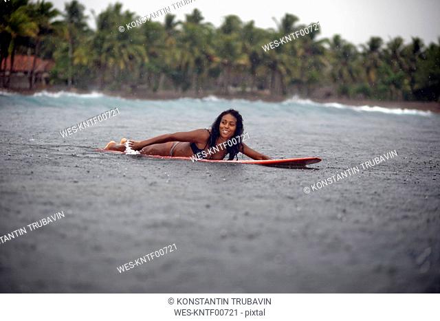 Indonesia, Java, woman lying on surfboard on the sea in rain