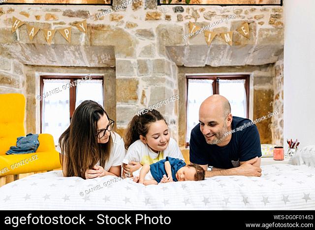 Parents and sister looking at new born baby while lying on bed at home