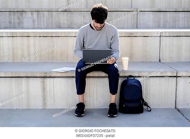 Man sitting on outdoor stairs using laptop