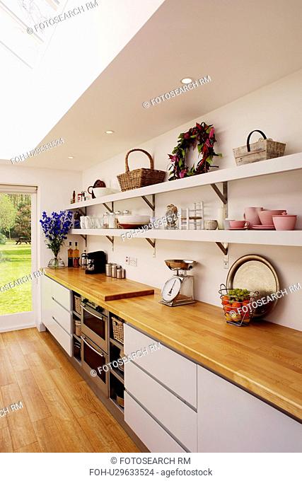 Wooden worktop on white fitted unit below shelves in modern white kitchen extension