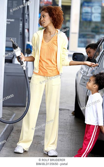 Black mother using pump at gas station