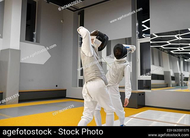 Two fencers exercising movements in duel at fencing room of professional martial art school