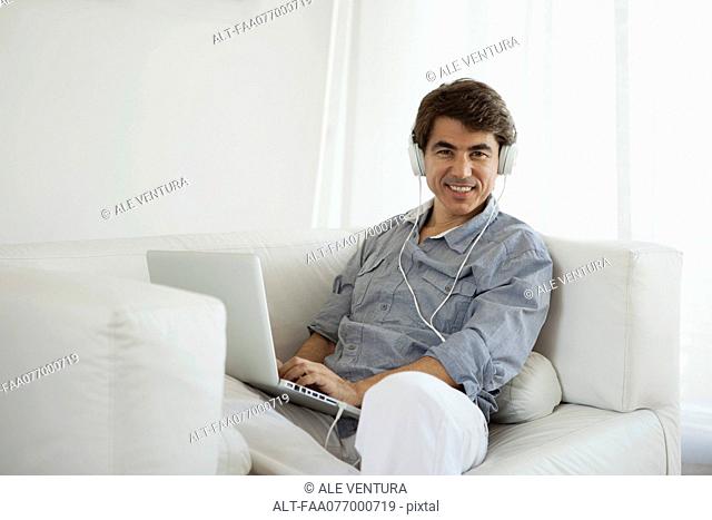 Mature man using laptop computer on sofa wearing headphones
