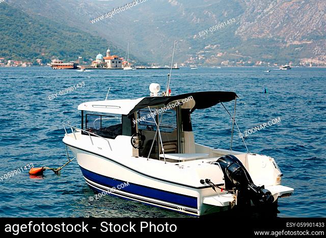 Motor boat moored near the town of Perast against the backdrop of the mountains and the island of Gospa od Skrpella. High quality photo