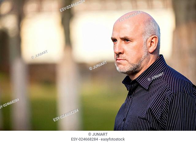 Confident attractive middle-aged man standing waiting in a rural lane with folded arms looking to the right hand side of the frame as though expecting somebody...