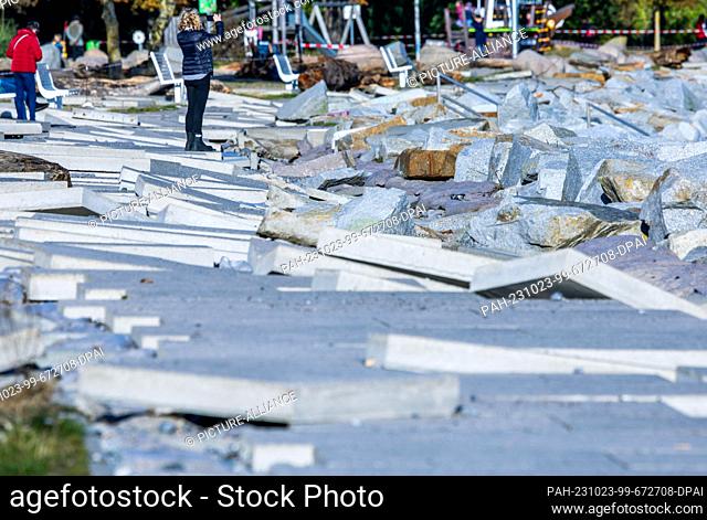 23 October 2023, Mecklenburg-Western Pomerania, Sassnitz: A woman takes a photo on the sidewalk slabs washed free by the storm surge on the Baltic Sea coast...