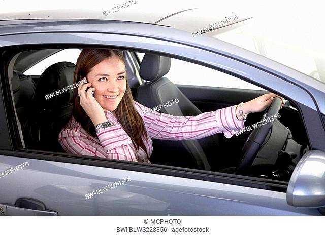 smiling young woman phoning with a mobile behind the steering wheel of a car