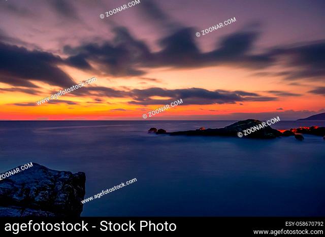 Rocky shore of the sea. Colorful sunset in the sky with clouds