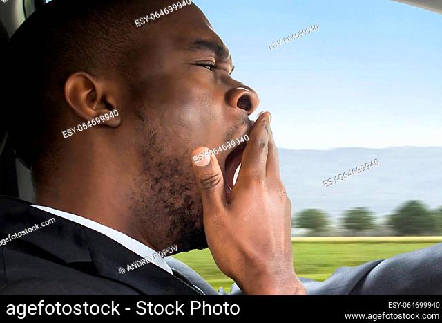 Side View Of A Young African Businessman Yawning While Driving Car