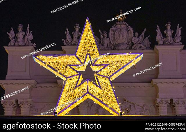 20 December 2022, Brandenburg, Potsdam: A yellow glowing poinsettia stands in Potsdam's city center on Luisenplatz against the backdrop of the Brandenburg Gate