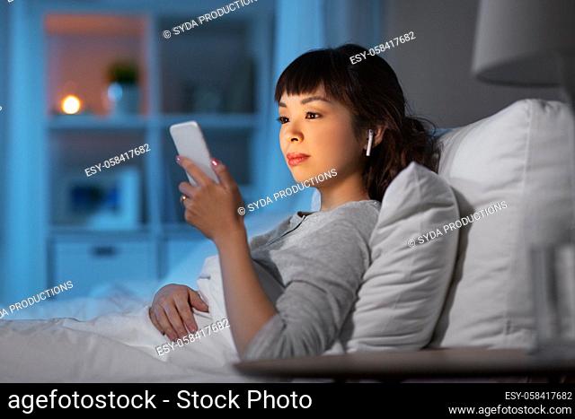 woman with phone and earphones in bed at night