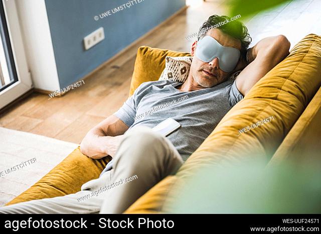 Man relaxing on sofa wearing eye mask at home