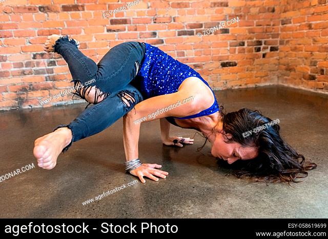 A determined and empowered woman shows strength and stamina as she holds her body in a twisted position through her hands, advanced handstand posture