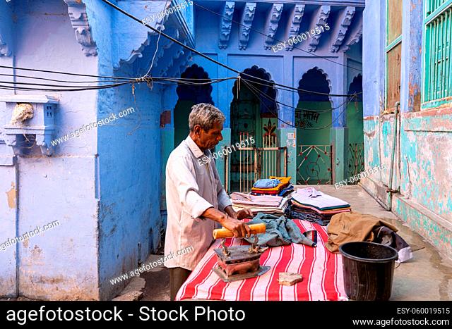 Jodhpur, India - December 9, 2019: A man is ironing clothes in between blue houses