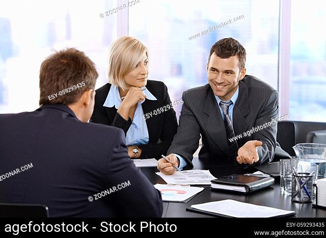 Smiling businessman discussing document at meeting with coworkers