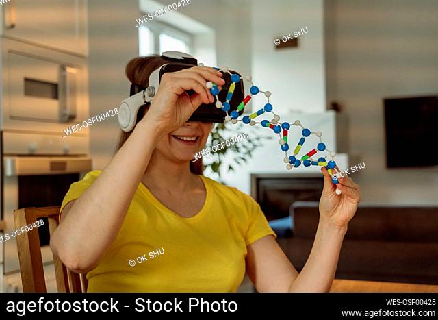Smiling woman wearing VR goggles and holding DNA model at home