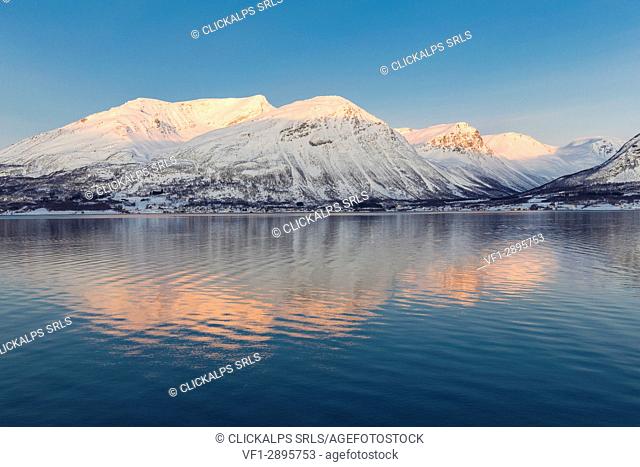 The peaks illuminated by the setting sun are reflected in Kafjorden. Kafjorden, Lyngen Alps, Troms, Norway, Lapland, Europe