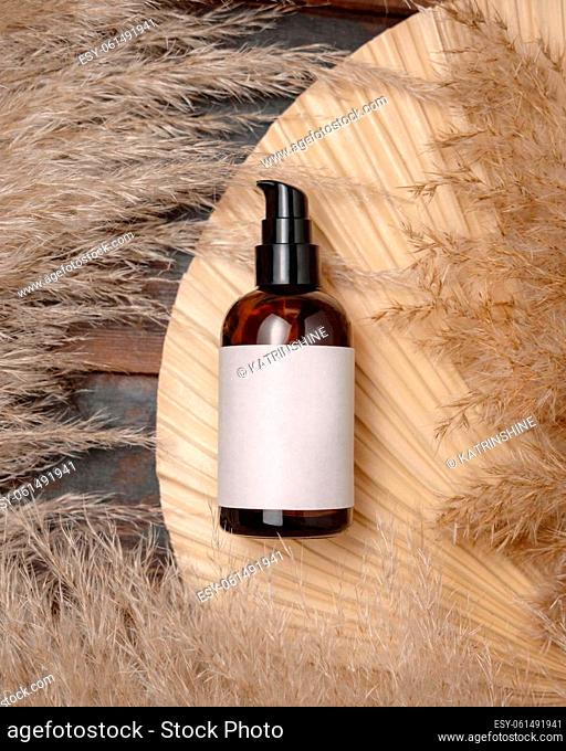 Cosmetic one pump bottle on dried palm leaf near pampas grass top view, label mockup. Skincare beauty product, lotion or essence