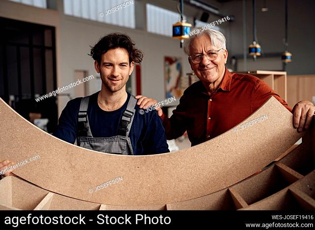 Smiling carpenter with businessman holding wooden plank at workshop