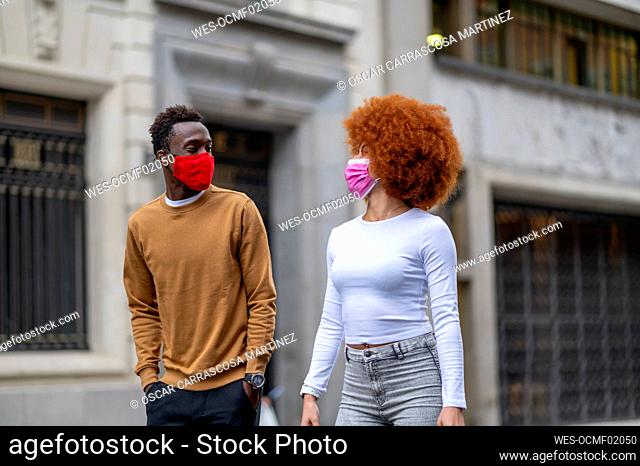 Couple wearing face mask looking at each other while walking in city