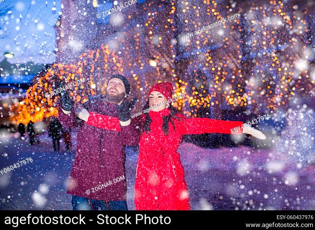 Adorable and happy young couple standing in a fairy-like cloud of snow, laughing. Portrait man and woman through the snowflakes on a foreground and city with...