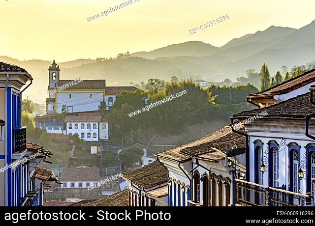 Facades of houses and church in colonial architecture in an old street in the city of Ouro Preto with the mountains in the background