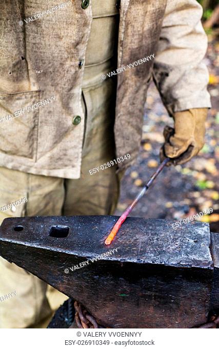 Blacksmith holds hot steel rod on anvil in outdoor rural smithy